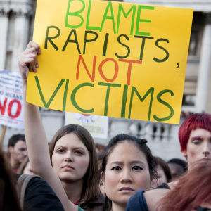 Nainen pitää mielenosoituksessa ylhäällä kylttiä jossa lukee: Syyttäkää raiskaajaa, älkää uhria 