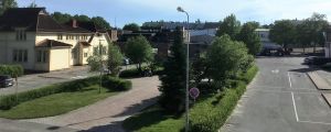 På andra sidan busstationsområdet och ett litet grönområde finns ungdomsgården i en gammal villa, Villa Haga. Tomma bussperronger, gator och ett gult gammalt trähus. Gräs och buskar, blå himmel, sommar.