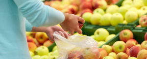 Person plockar frukter i plastpåse. I bakgrunden syns flera lådor av äpplen.