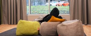 Elisa trivs med lärarna och terapeuterna i Laustis. En ung person sitter med en grå munkjacka med huvan dragen över huvudet. Personen har ryggen mot kameran och tittar ut genom ett fönster på en regnig parkeringsplats.