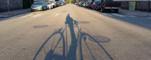 Skuggan av en cyklist över asfalten en tidig sommarmorgon i trähusstadsdelen Port Arthur i Åbo.