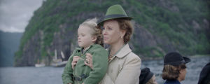 En liten trasnportbåt. Ombord ser vi Märtha som håller i sonen Harald och de tittar båda framåt.