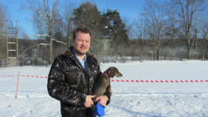 Olli Muurainen är förvånad över myndigheternas agerande. man med hund i famnen i vinterlandskap.