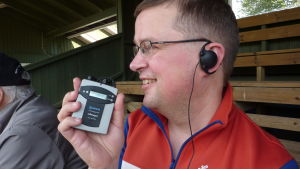 Jan-Peter Sjöholm får fotbollsmatchen syntolkad. Jan-Peter Sjöholm visar apparaten som gör att han hör syntolkningen.