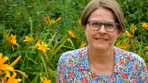Heidi Hautala. Heidi Hautala på en sommaräng omgiven av gula blommor