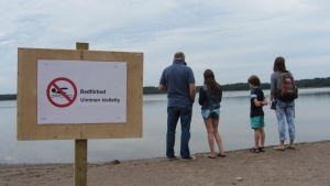Det var badförbud vid Knipans badstrand sommaren 2014 på grund av kolibakterier. familj på strand invid skylt med badförbud