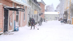 Vintern kom till Mellangatan i Borgå. En kvinna sopar bort snön utanför sin affär i Borgås Gamla stan.