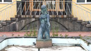 Så här säg Eurydike ut före renoveringen. En staty, kvinnlig figur, i en liten ljusblå bassäng utan vatten, sand och löv och vattenrör syns på bassängbottnen.