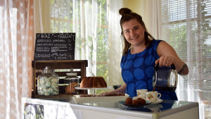 Emilia Nyberg har redan hunnit servera kaffe till många kaffetörstiga cafégäster. Emilia Nyberg står och häller kaffe i två kaffekoppar. På disken står flera fat med kakor och andra bakverk.