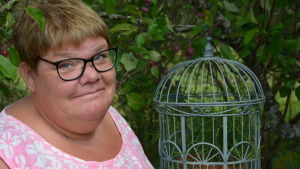 Susanne Gustafsson. Susanne Gustafsson står nära en fågelbur med växtlighet.