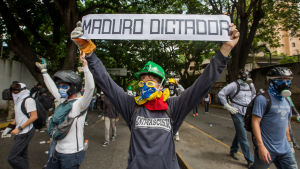 Långt över hundra människor har dödats i regeringskritiska demonstrationer som pågått sedan april. "Maduro är diktator" står det på den här unga demonstrantens banderoll. 1.5.2017