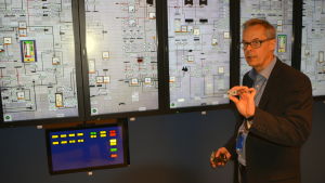 Att simulatorn är digital är delvis en kostnadsfråga. Ulf Lindén säger att det är mycket billigare att använda pekskrämar och mjukvara än att använda analoga brytare som i det riktiga kontrollrummet. Ulf Lindén håller upp en analog brytare framför en pekskärm i Lovisa kärnkraftverks simulator.