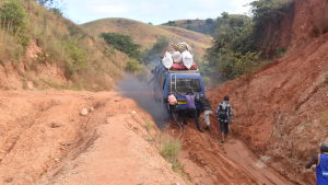 Passagerare hjälper till med att få en lokal buss uppför en sandig och dammig backe i Madagaskar.