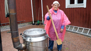 När gröten kokar i fältköket måste marthorna röra runt med enorma träslevar. En kvinna iklädd rosa regnrock håller i en stor slev vid ett fältkök i rostfritt stål.