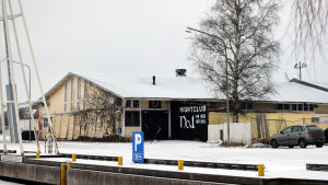 I dag finns det en nattklubb i magasinet. En gul gammal magasinbyggnad i Ekenäs norra hamn. På ena sidan syns en björk. Marken är täckt av snö.