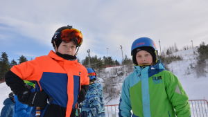 Jesse Kuoppala och Jeri Backholm Jesse Backholm står till vänster, han har stora skidglasögon över pannan och en orange och blå jacka. Till höger som Jeri Kuoppala med en grön och blå jacka och en blå hjälm på huvudet. De står i liftkön till Öjberget.