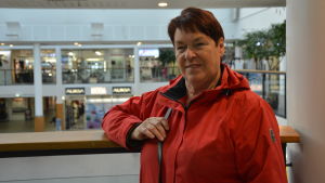 Leena Rautavalta. Leena Rautavalta har mörkrött, kort hår och en röd jacka. Hon är i 70-årsåldern och står på Rewell Centers andra våning.