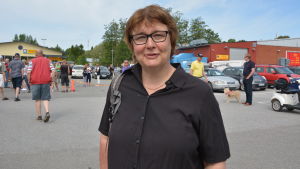 Christa Perämaa-Bredenberg flaggar lokalt då det kommer till nypotatis. Medelålders kvinna med rödbrunt hår och glasögon samt svart skjorta njuter av sommarvärmen i södra hamnen i Nagu.