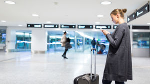 Räknar man med all väntetid så kan tåget vara ett snabbare alternativ än flyget. En kvinna står på ett flygfält och tittar på sin mobil, med kappsäcken framför sig.