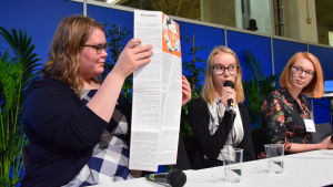 Rebecca Mattbäck håller upp en novellaffisch, en berättelse i planschformat. Person i paneldiskussion håller upp en plansch.