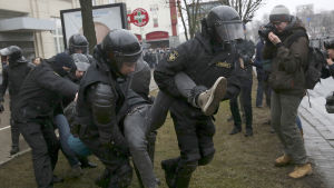 Säkerhetspolisen bär en demonstrant i Minsk. Till höger står en journalist och fotograferar händelsen.