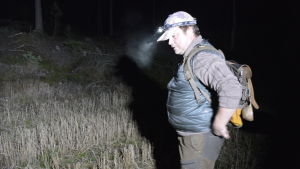 Tommy Arfman på väg ut i skogen. Jägare med pannlampa och ryggsäck i mörk skog.