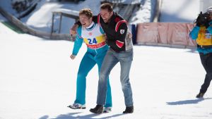 Taron Egerton och Hugh Jackman lämnar jublande hoppbacken med en kameraman i hälarna.