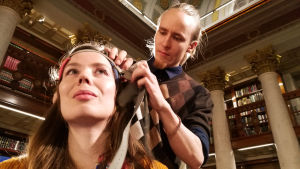 Prisma Studion toimittaja Henna-Leena Kallio testaa tasavirtastimulaatiota. Tohtorikoulutettava Aaron Kortteenniemi asentaa tDCS-laitetta. Tohtorikoulutettava Aaron Kortteenniemi asentaa tDCS-laitetta Prisma Studion toimittaja Henna-Leena Kalliolle.