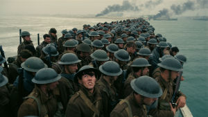 Den långa piren i Dunkirk är full av väntande soldater. En soldat står på en överfylld pir tittar upp mot himlen.