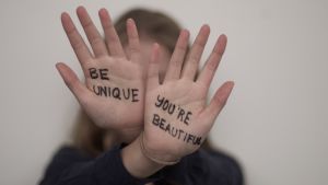 Två händer som hålls upp med texten "be unique" och "you're beautiful" skrivna på handflatorna.
