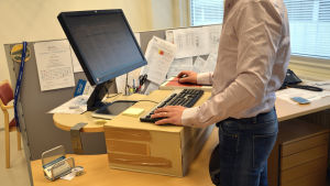 Papplåda under tangentbordet. Inte så snyggt kanske, men praktiskt. En man har höjt upp sitt skrivbord med en låda under tangentbordet.