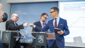 Jari Lindström, Juha Sipilä och Alexander Stubb firar samhällsfördraget med en fist bump, en grabbhälsning. Jari Lindström, Juha Sipilä och Alexander Stubb