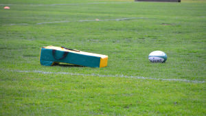 Plastdyna och rugbyboll. Dynan används under träningarna och uppvärmningen före matcher då spelare springer mot varandra. gul plastdyna och avlång rugbyboll på gräsplan.