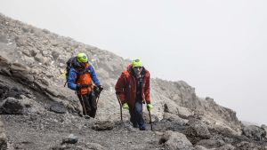 Aron Anderson tar hjälp av kryckor när han klättrar i berg, som här på Kilimanjaro, år 2016. Aron Anderson och en till bergsklättrare, som går uppför ett berg. Aron har kryckor.