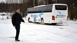 Fredrik Ström. Fredrik Ström går framför en buss som körs av bolaget Wasabus. På en parkering. Vinter.