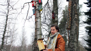 Perttu Matero Suomen Metsästysmuseosta seisoo ulkona koivujen katveessa ja pitelee kädessään linnunpönttöä.