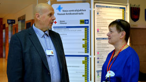 Göran Honga, direktör för Vasa sjukvårdsdistrik och Ann-Katrin Brandtberg, förman på akuten vid Vasa Centralsjukhus. Göran Honga och Ann-Katrin Brandtberg står och diskuterar i aulan på Vasa centralsjukhus.