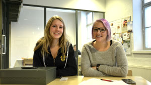 Josefine Sundblom och Matilda Skrifvars. Josefine Sundblom och Matilda Skrifvars sitter vid ett bord där de har ett kassaskrin, papper, penna och en telefon.