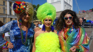 Tre pridedeltagare klädda i färggranna och glittrande kläder och peruker under Helsingfors prideparad 2016.