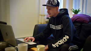 Alex letar efter lediga jobb. Det finns inte så många, speciellt för en som inte har bil. Alex Granqvist sitter i en soffa och använder dator.