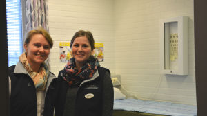 Nina Herrgård och Marion Salmela. Skolhälsovårdarna Nina Herrgård och Marion Salmela står i sitt mottagningsrum på Korsholms högstadium. De har blåa jackor på sig och skarfar runt halsen.