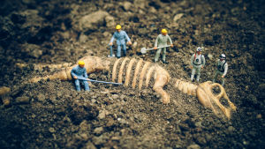 Pienet muovihahmot kaivavat dinosauruksen luurankoa esiin hiekasta.