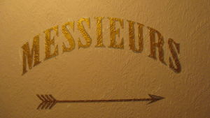 Seinään maalattu ranskankielinen teksti messieurs ja nuoli, jotka ohjaavat miestenhuoneeseen