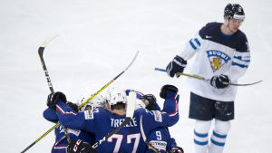 Finland mot Frankrike En besviken finsk ishockeyspelare med jublande franska spelare i förgrunden.