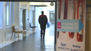 Man går i korridor på Vasa centralsjukhus förbi en affisch som pekar ut var provtagningen och laboratoriet finns.