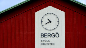 Bergö skola. Bild av Bergö skolas yttervägg där det finns en stor klocka och texten Bergö skola bibliotek.