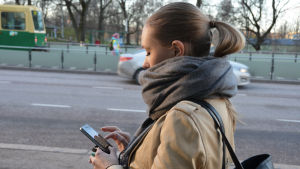 Mobilbetalningar är fortfarande rätt ovanliga i Finland. Kvinna går på stan och kollar på sin smarttelefon.