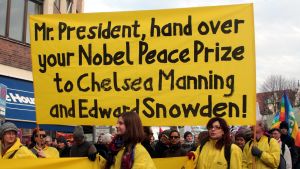 Tyska demonstranter uppmanar, vid en säkerhetskonferens 2014, USA:s dåvarande president Barack Obama att överräcka sitt Nobels fredspris till visselblåsarna Chelsea Manning och Edward Snowden. Gulklädda demonstranter bär en skylt med texten: Mr. President, hand over your Nobel Peace Prize to Chelsea Manning and Edward Snowden.