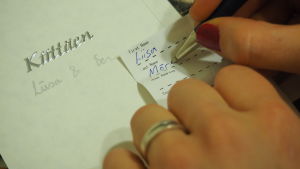 Nainen kirjoittaa nimeään paperiin, häiden kiitoskortti taustalla.