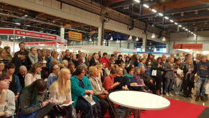 Mässpublik kring Märta Tikkanen. Märta Tikkanen intervjuad av nina nyman samlar publik på bokmässan i helsingfors 2015.